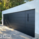 A modern contemporary architectural home with flush-mounted metal paneled garage doors. The double-car and single-car garage doors features horizontal metal panels that camouflage into the surrounding metal clad wall panels around the garage door openings. Both flush mount garage doors are finished in matte black to blend in seamlessly with the architectural paneling of this Beverly Hills home.