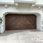 Authentic Spanish Colonial double-car garage door in clear vertical grain cedar. The garage door features a Herringbone tongue and groove plank design with perimeter trim work. The corner portion of the trim mimics the home's existing corbel designs. One-third from the bottom is a horizontal trim piece the finishes off the carriage door design of the door. Alone or with decorative iron hardware this door is a fabulous design for a Santa Barbara style home!